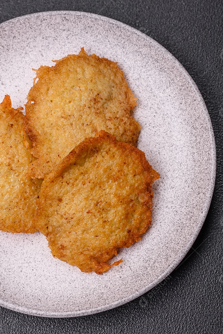 Deliciosas panquecas crocantes feitas de batatas, carne, cenouras, cebolas com sal, especiarias e ervas sobre um fundo escuro de concreto