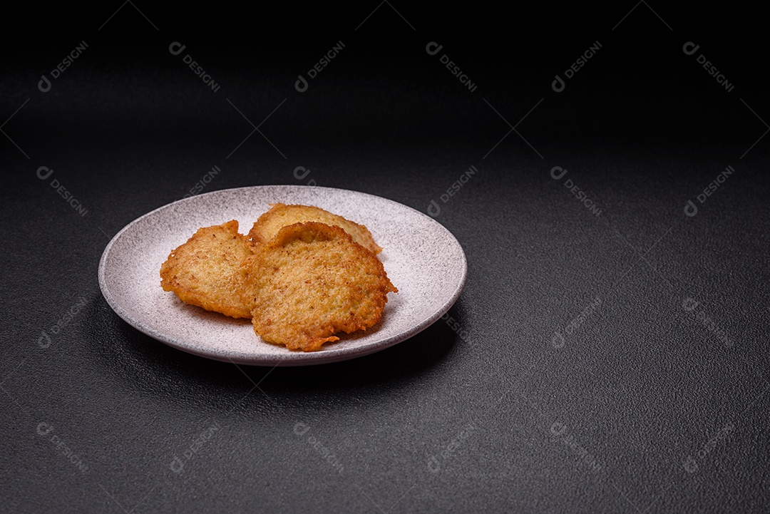 Deliciosas panquecas crocantes feitas de batatas, carne, cenouras, cebolas com sal, especiarias e ervas sobre um fundo escuro de concreto