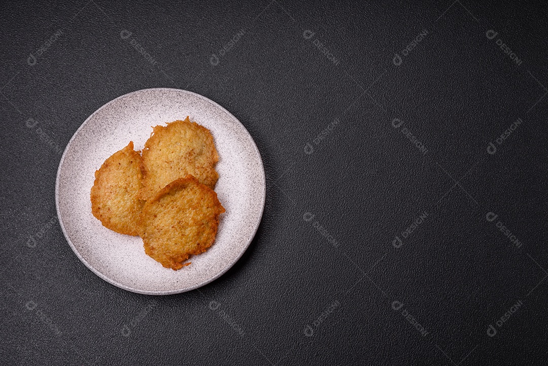 Deliciosas panquecas crocantes feitas de batatas, carne, cenouras, cebolas com sal, especiarias e ervas sobre um fundo escuro de concreto