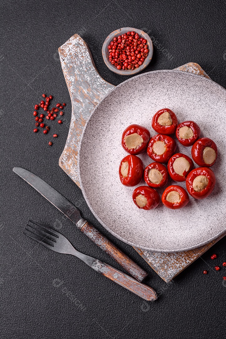 Pimentões vermelhos recheados com queijo ou carne com sal, especiarias e ervas num prato de cerâmica