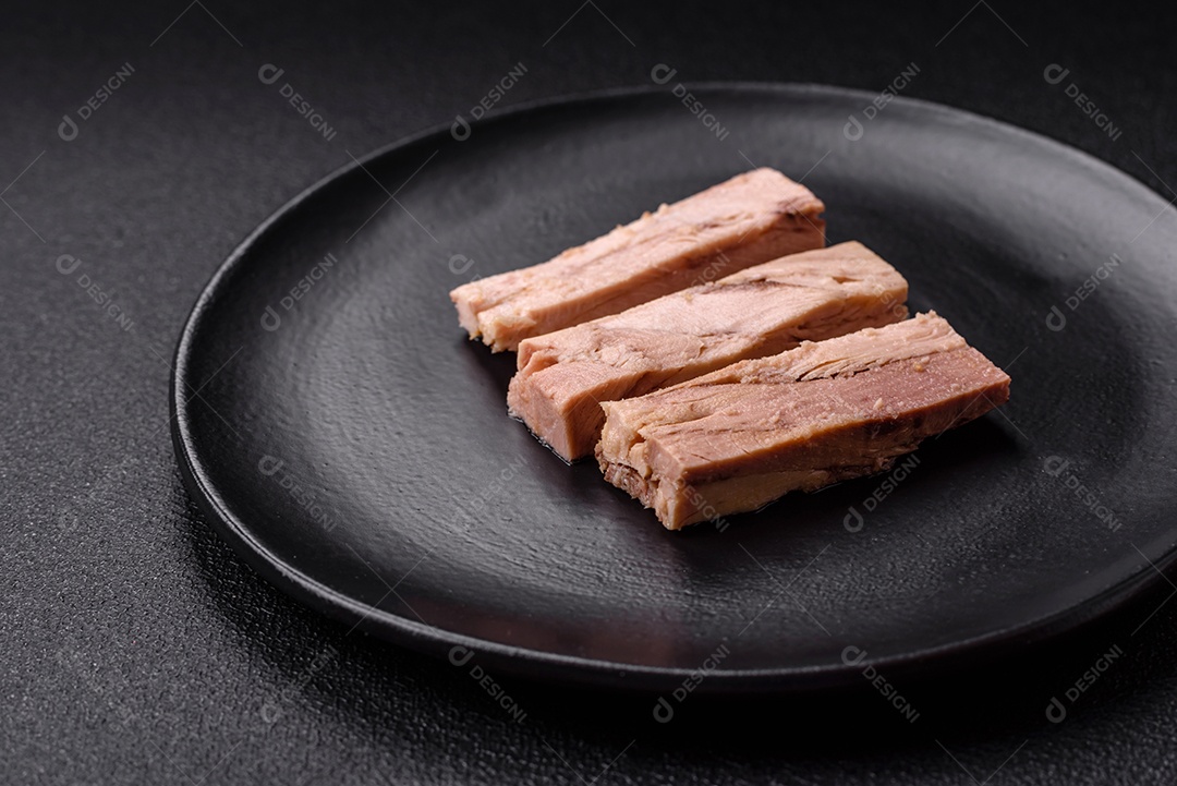 Deliciosa carne de atum dietético enlatado com sal, especiarias e óleo sobre um fundo escuro de concreto