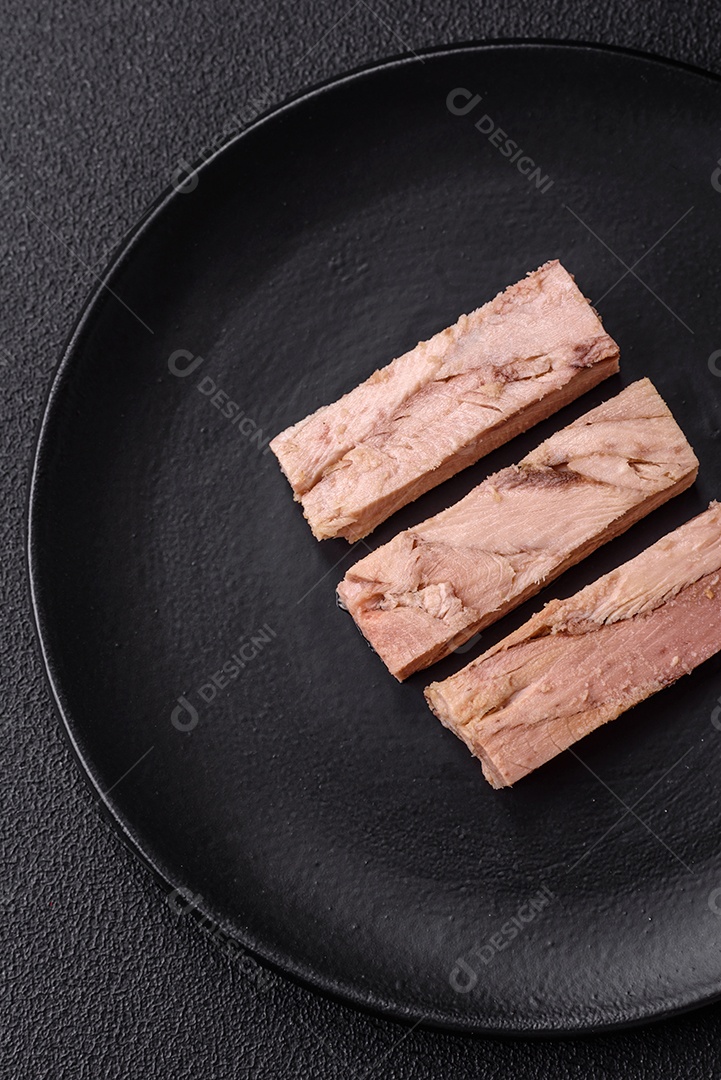 Deliciosa carne de atum dietético enlatado com sal, especiarias e óleo sobre um fundo escuro de concreto