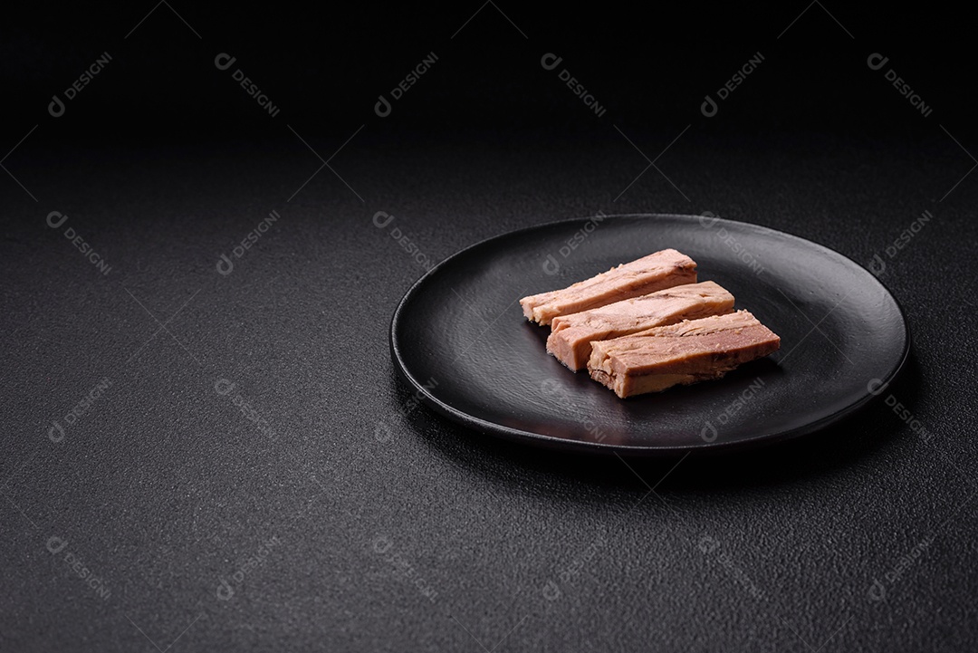 Deliciosa carne de atum dietético enlatado com sal, especiarias e óleo sobre um fundo escuro de concreto