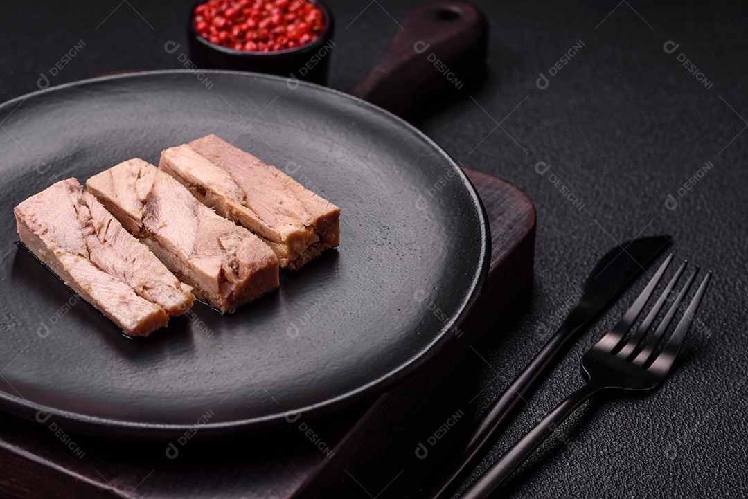 Deliciosa carne de atum dietético enlatado com sal, especiarias e óleo sobre um fundo escuro de concreto