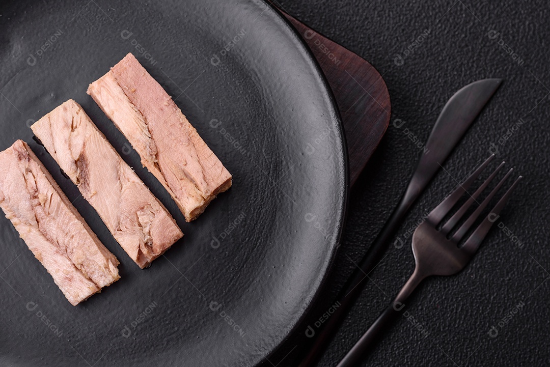Deliciosa carne de atum dietético enlatado com sal, especiarias e óleo sobre um fundo escuro de concreto