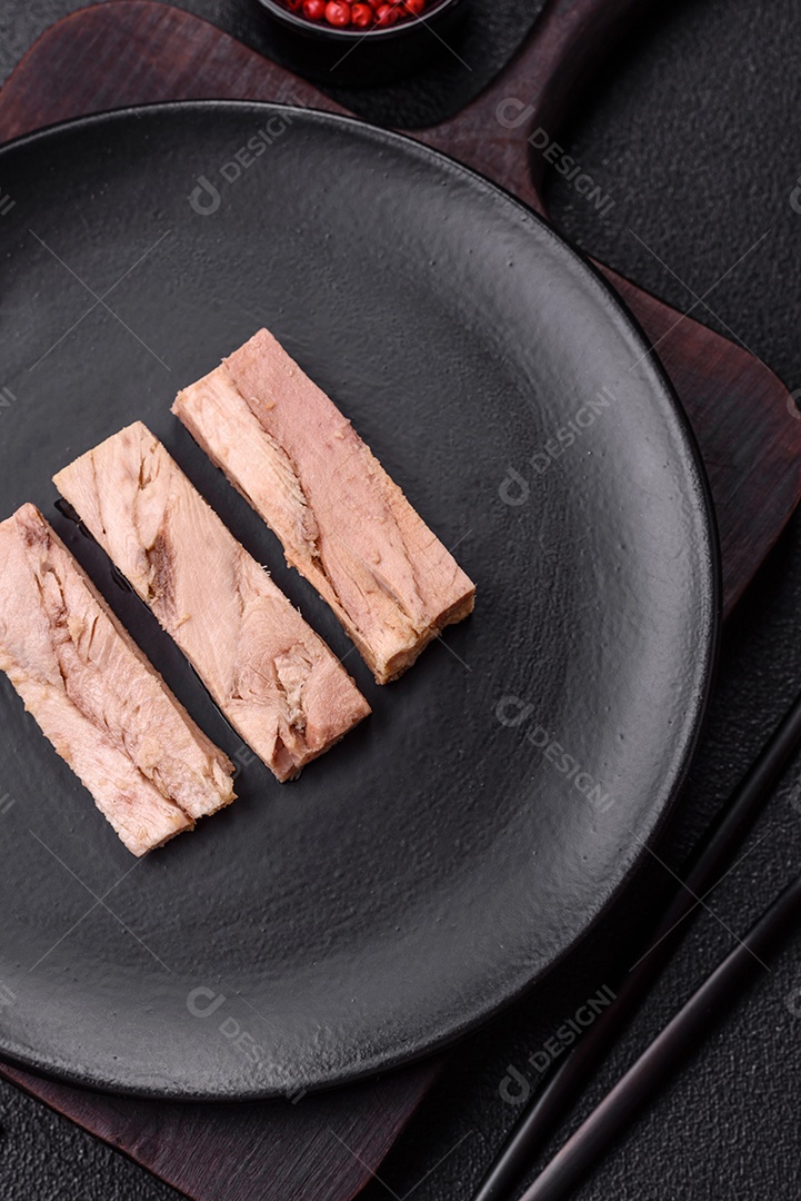 Deliciosa carne de atum dietético enlatado com sal, especiarias e óleo sobre um fundo escuro de concreto