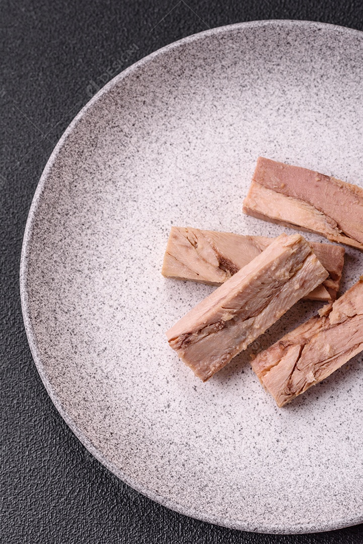 Deliciosa carne de atum dietético enlatado com sal, especiarias e óleo sobre um fundo escuro de concreto