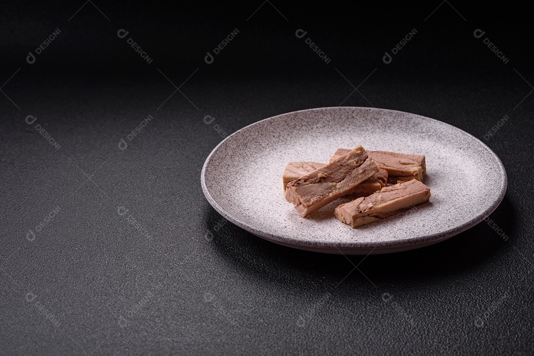 Deliciosa carne de atum dietético enlatado com sal, especiarias e óleo sobre um fundo escuro de concreto