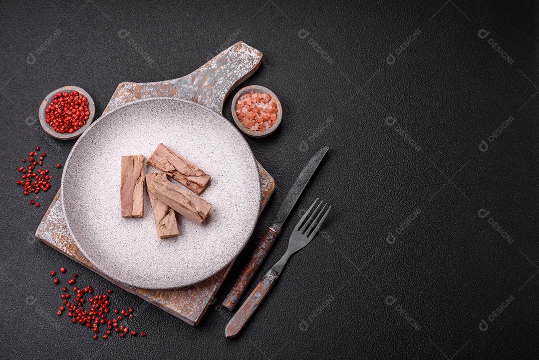 Deliciosa carne de atum dietético enlatado com sal, especiarias e óleo sobre um fundo escuro de concreto