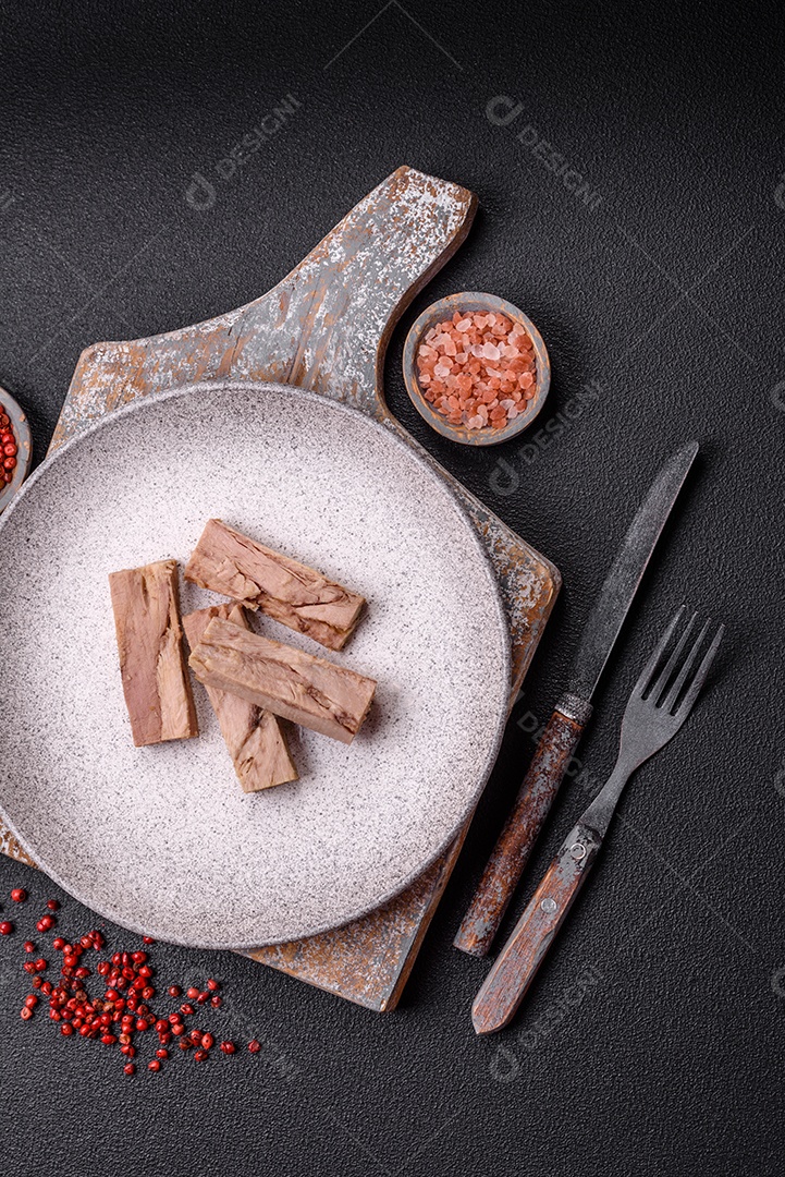 Deliciosa carne de atum dietético enlatado com sal, especiarias e óleo sobre um fundo escuro de concreto