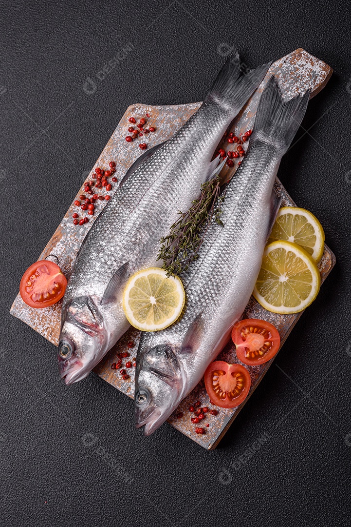 Peixe fresco de robalo oceânico cru com sal, especiarias e ervas em fundo de concreto escuro