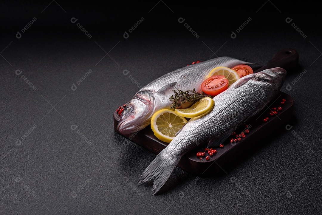 Peixe fresco de robalo oceânico cru com sal, especiarias e ervas em fundo de concreto escuro