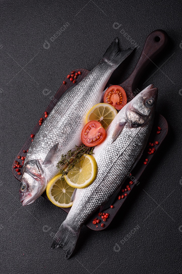 Peixe fresco de robalo oceânico cru com sal, especiarias e ervas em fundo de concreto escuro