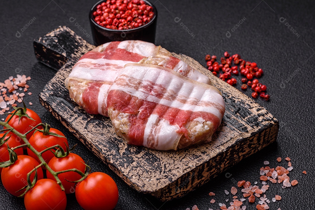Frango picado redondo ou costeleta de porco envolta em bacon com sal, especiarias e ervas sobre um fundo escuro de concreto
