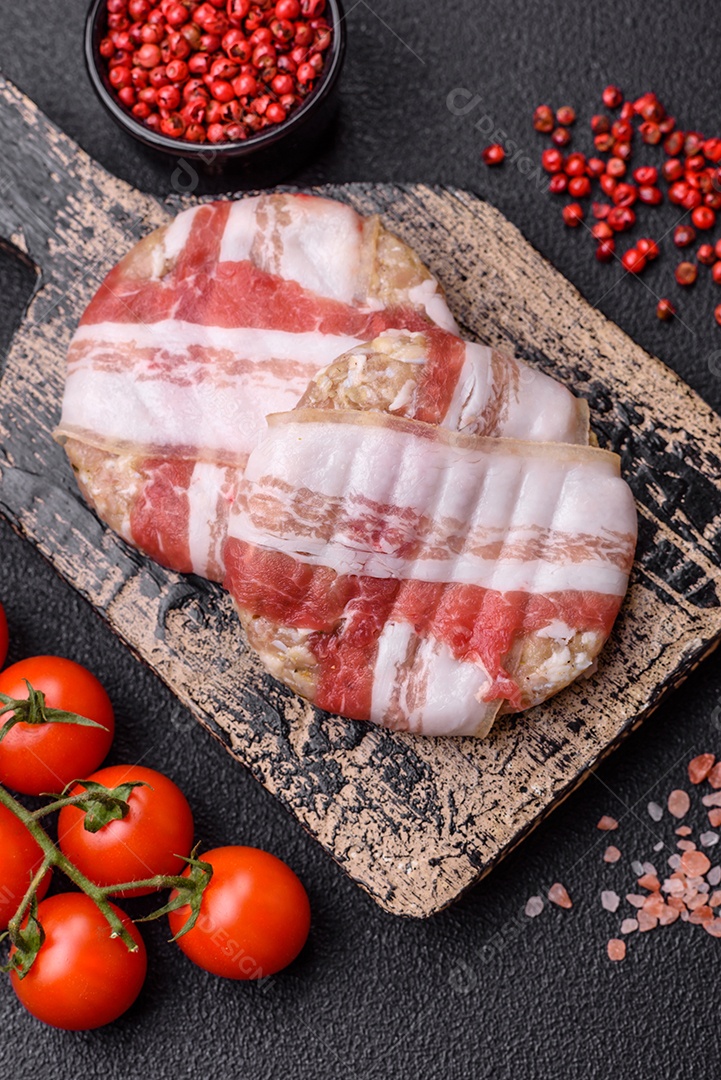 Frango picado redondo ou costeleta de porco envolta em bacon com sal, especiarias e ervas sobre um fundo escuro de concreto