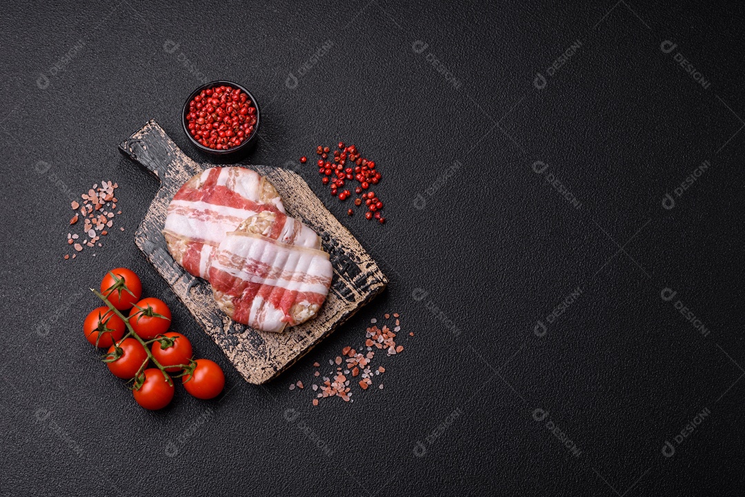 Frango picado redondo ou costeleta de porco envolta em bacon com sal, especiarias e ervas sobre um fundo escuro de concret