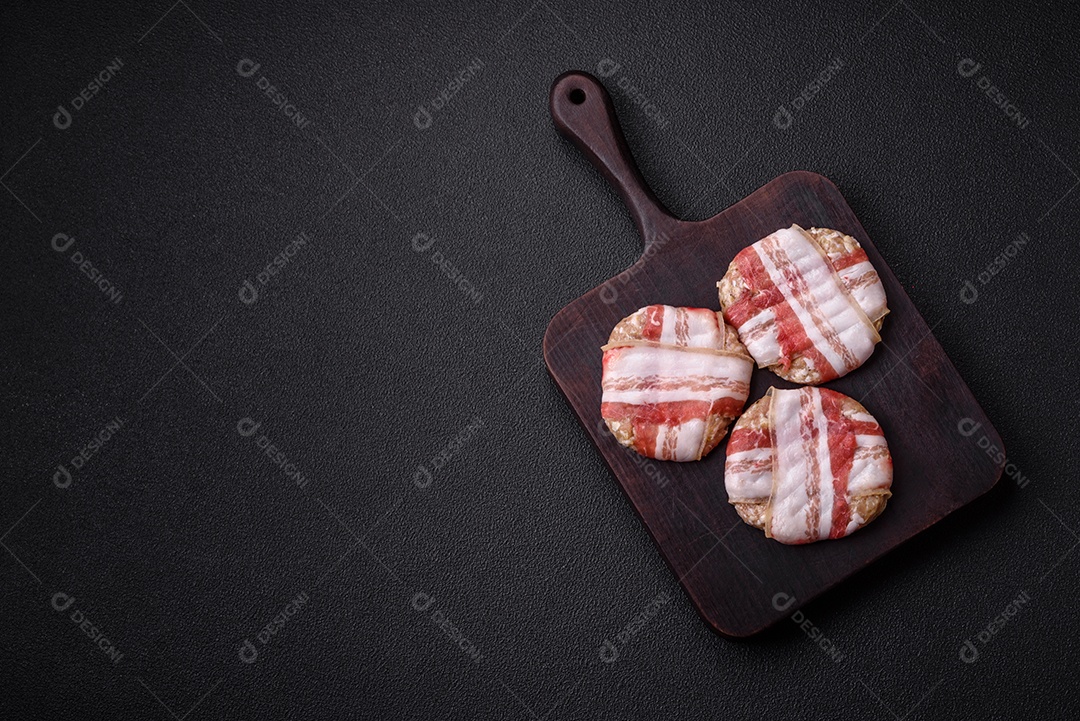 Frango picado redondo ou costeleta de porco envolta em bacon com sal, especiarias e ervas sobre um fundo escuro de concreto