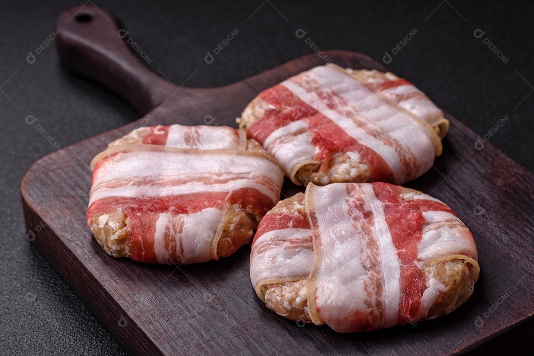 Frango picado redondo ou costeleta de porco envolta em bacon com sal, especiarias e ervas sobre um fundo escuro de concreto
