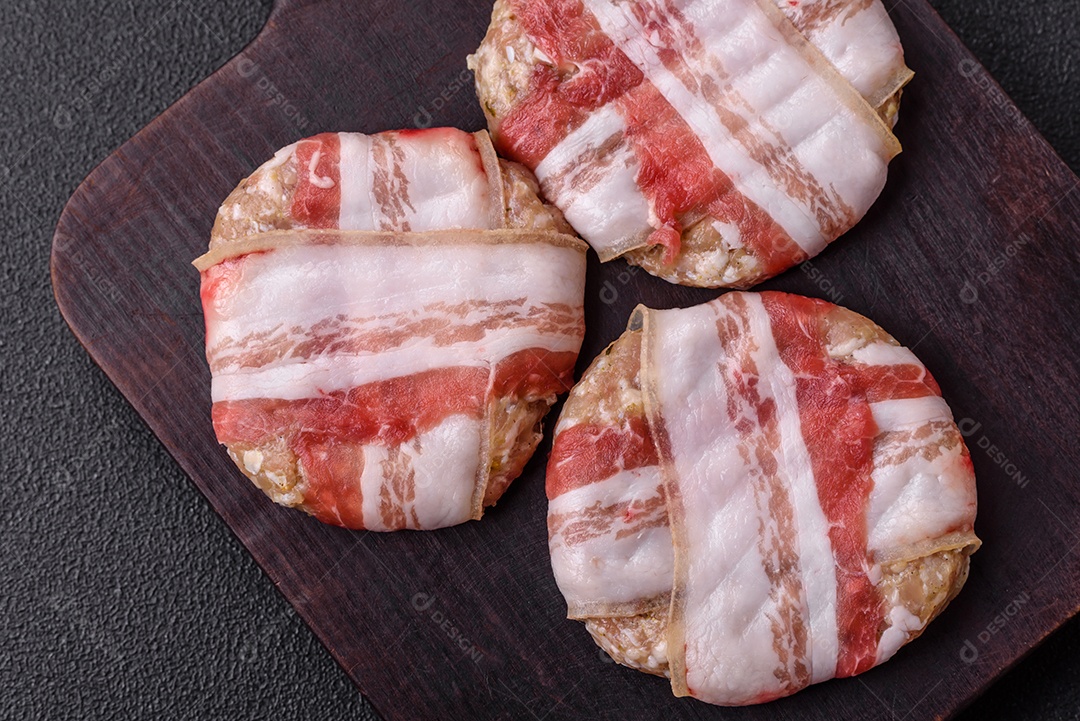 Frango picado redondo ou costeleta de porco envolta em bacon com sal, especiarias e ervas sobre um fundo escuro de concreto