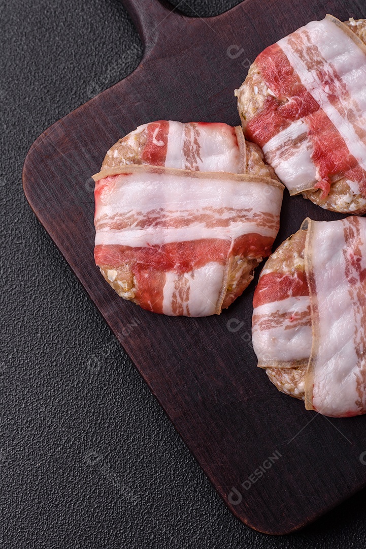 Frango picado redondo ou costeleta de porco envolta em bacon com sal, especiarias e ervas sobre um fundo escuro de concreto