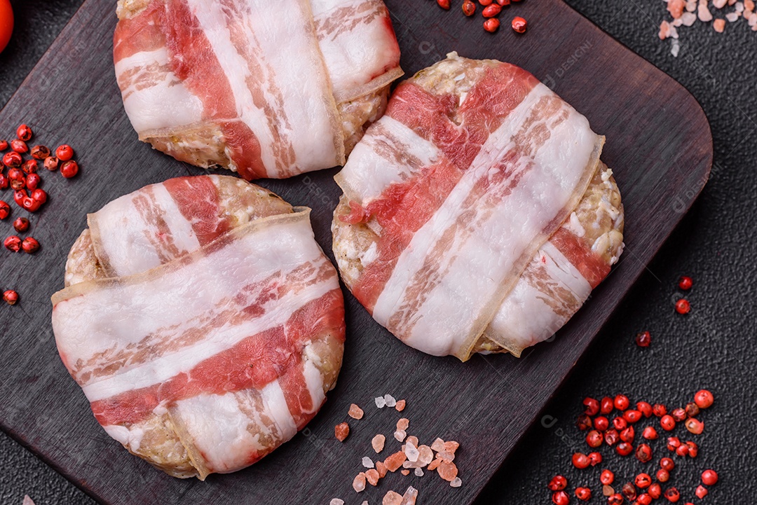 Frango picado redondo ou costeleta de porco envolta em bacon com sal, especiarias e ervas sobre um fundo escuro de concreto