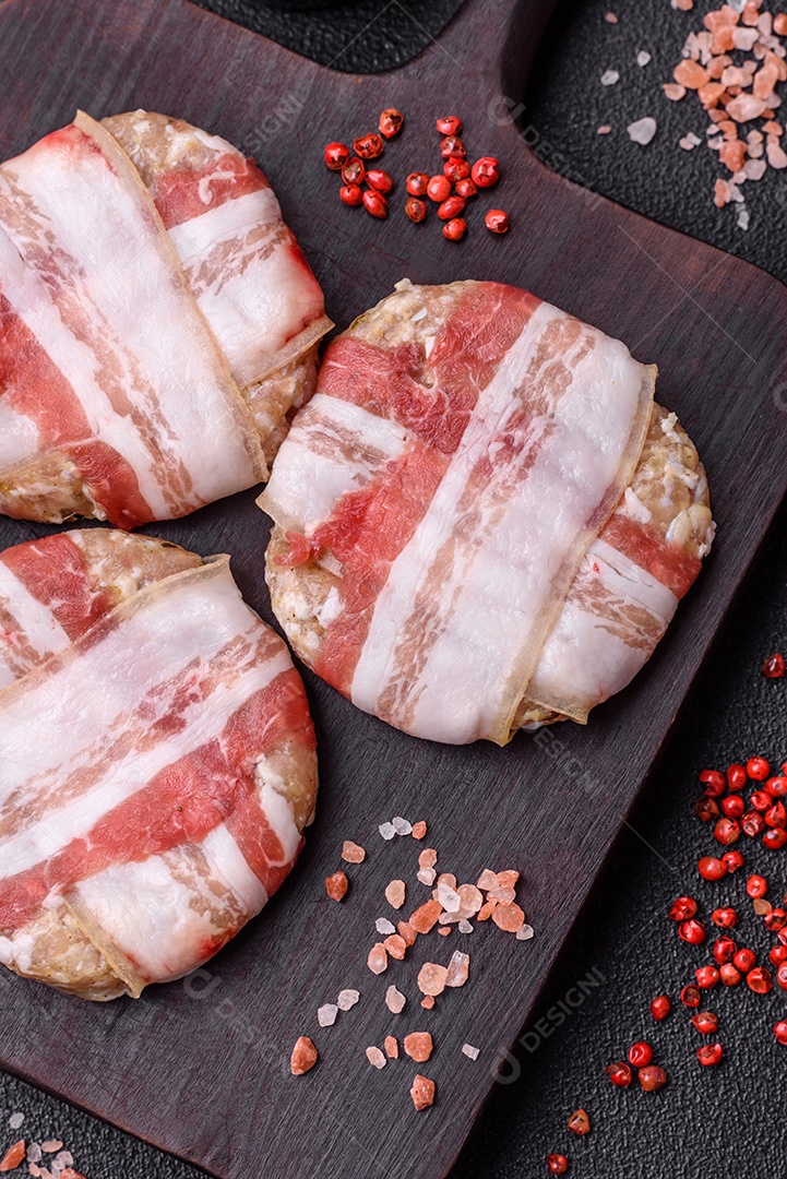 Frango picado redondo ou costeleta de porco envolta em bacon com sal, especiarias e ervas sobre um fundo escuro de concreto
