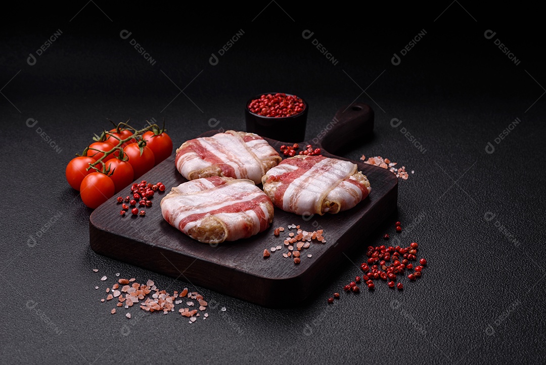 Frango picado redondo ou costeleta de porco envolta em bacon com sal, especiarias e ervas sobre um fundo escuro de concreto