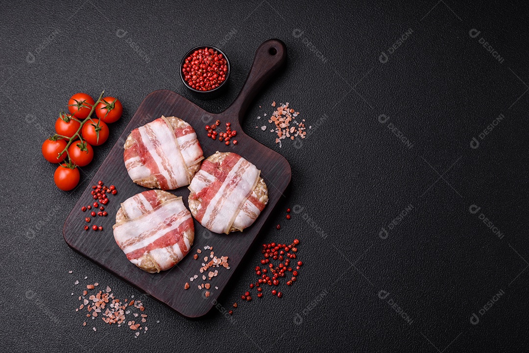 Frango picado redondo ou costeleta de porco envolta em bacon com sal, especiarias e ervas sobre um fundo escuro de concreto