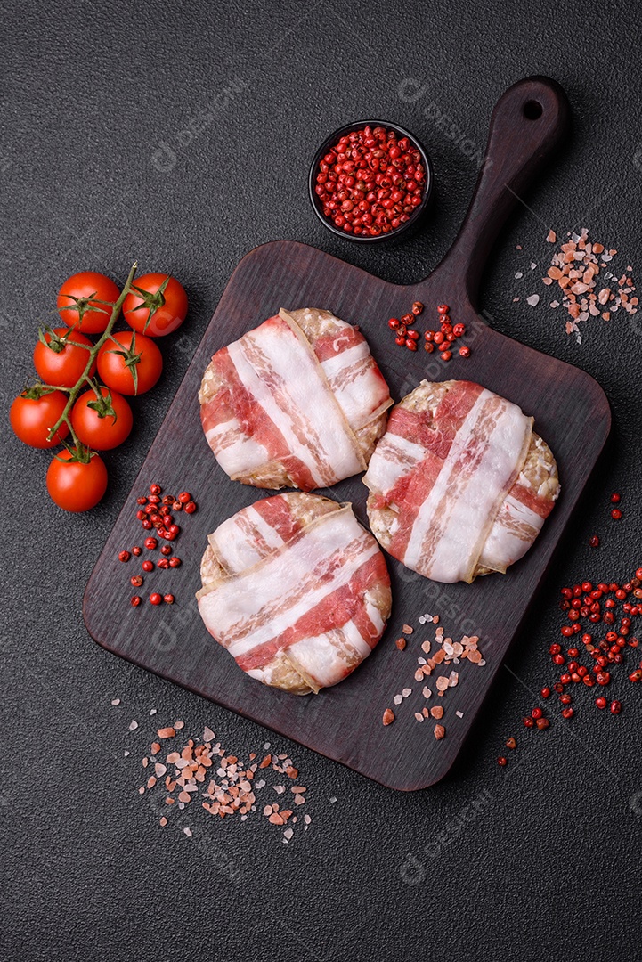 Frango picado redondo ou costeleta de porco envolta em bacon com sal, especiarias e ervas sobre um fundo escuro de concreto