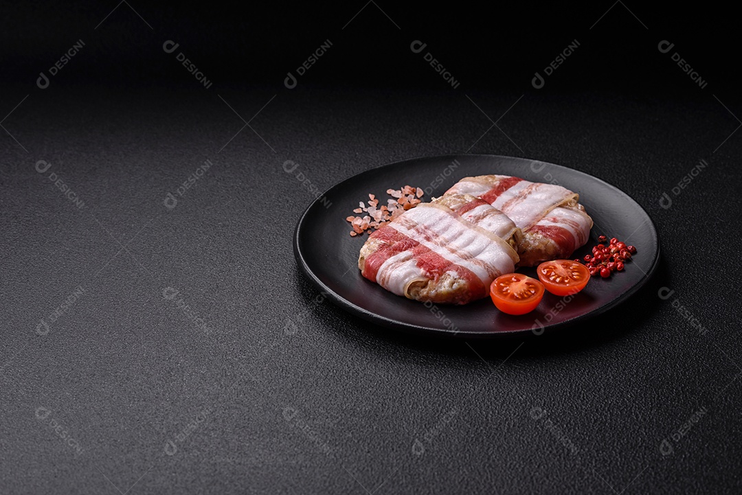 Frango picado redondo ou costeleta de porco envolta em bacon com sal, especiarias e ervas sobre um fundo escuro de concreto