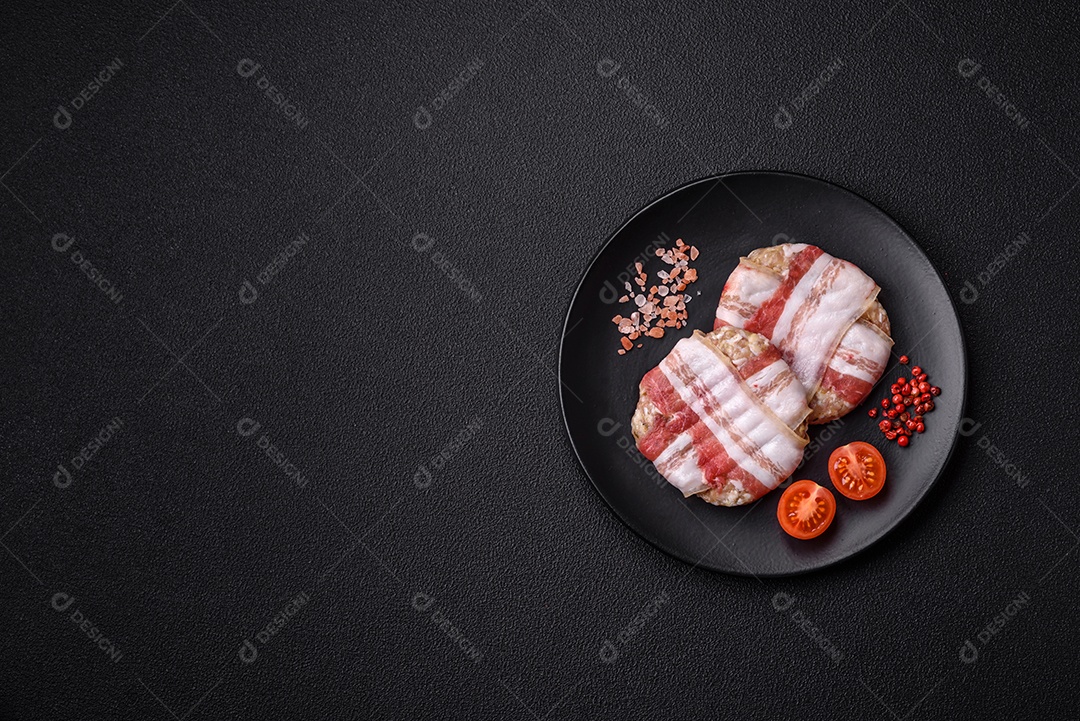 Frango picado redondo ou costeleta de porco envolta em bacon com sal, especiarias e ervas sobre um fundo escuro de concreto