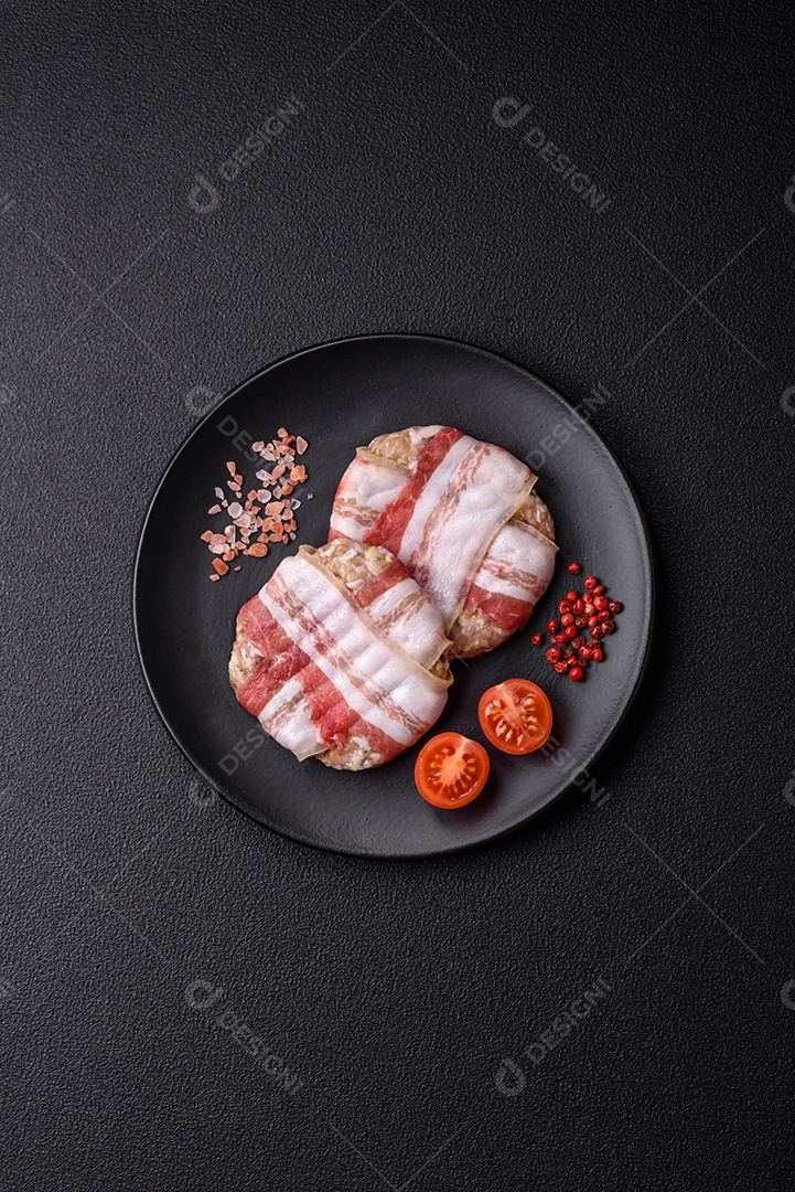 Frango picado redondo ou costeleta de porco envolta em bacon com sal, especiarias e ervas sobre um fundo escuro de concreto
