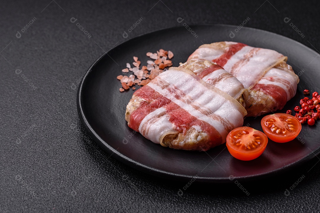 Frango picado redondo ou costeleta de porco envolta em bacon com sal, especiarias e ervas sobre um fundo escuro de concreto