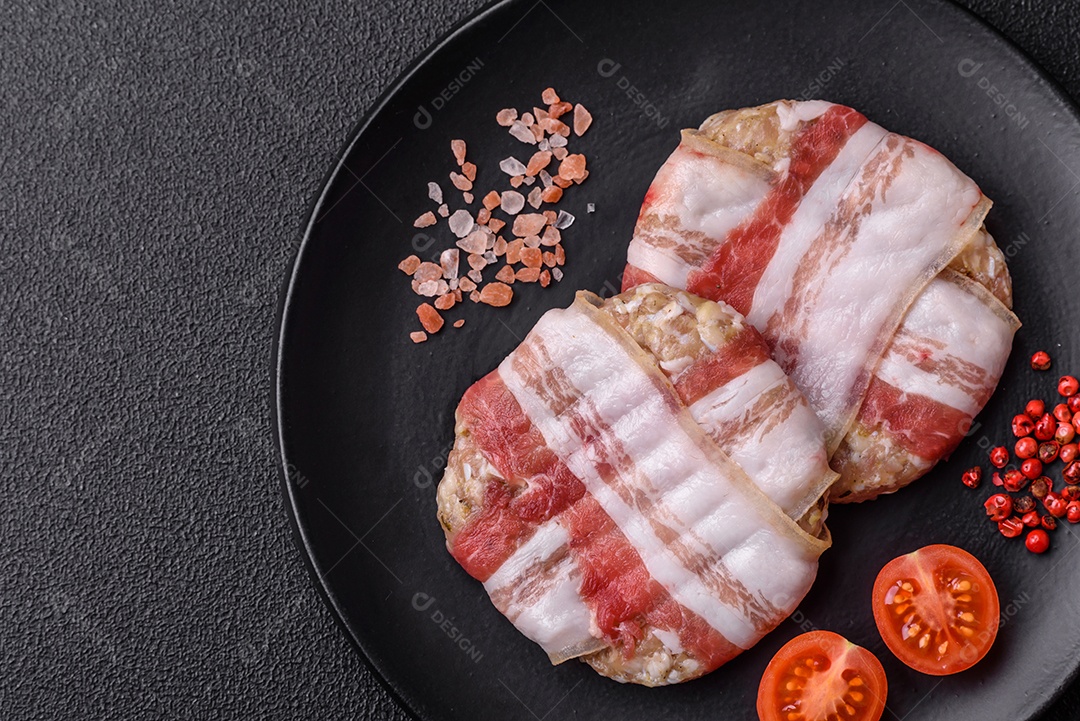 Frango picado redondo ou costeleta de porco envolta em bacon com sal, especiarias e ervas sobre um fundo escuro de concreto