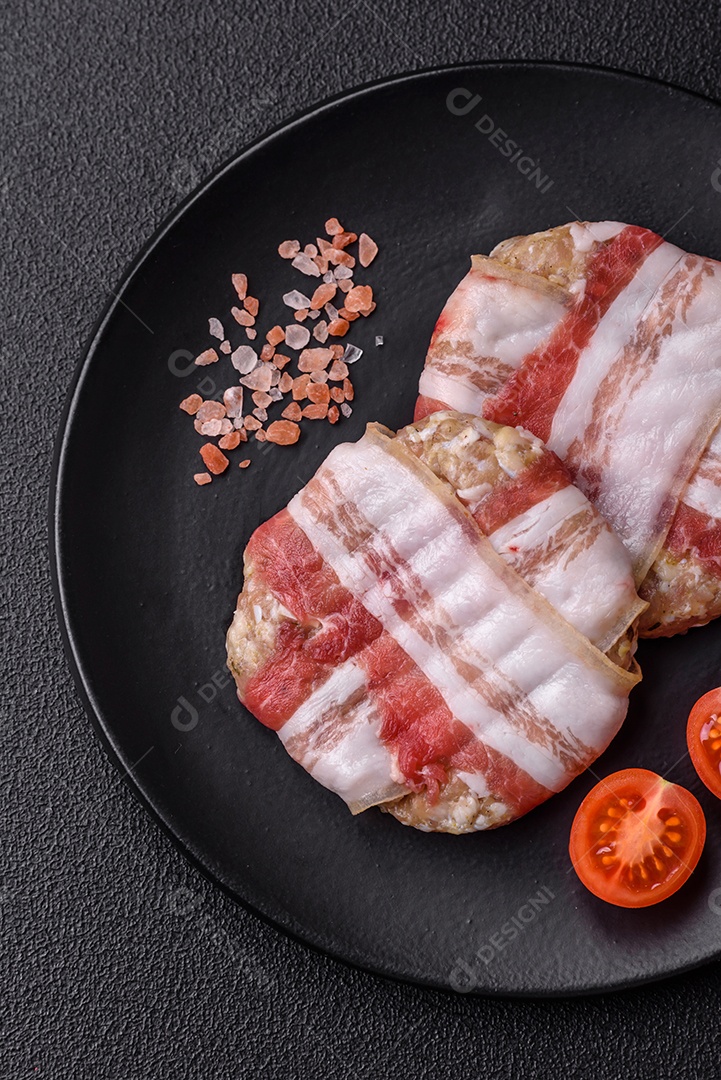 Frango picado redondo ou costeleta de porco envolta em bacon com sal, especiarias e ervas sobre um fundo escuro de concreto