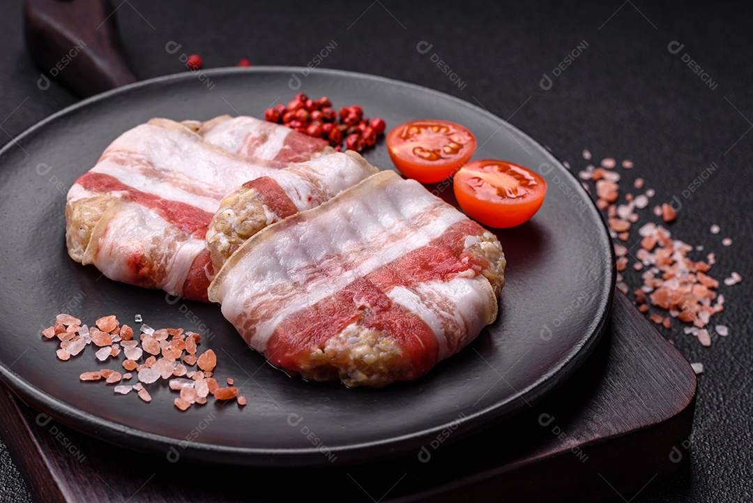 Frango picado redondo ou costeleta de porco envolta em bacon com sal, especiarias e ervas sobre um fundo escuro de concreto