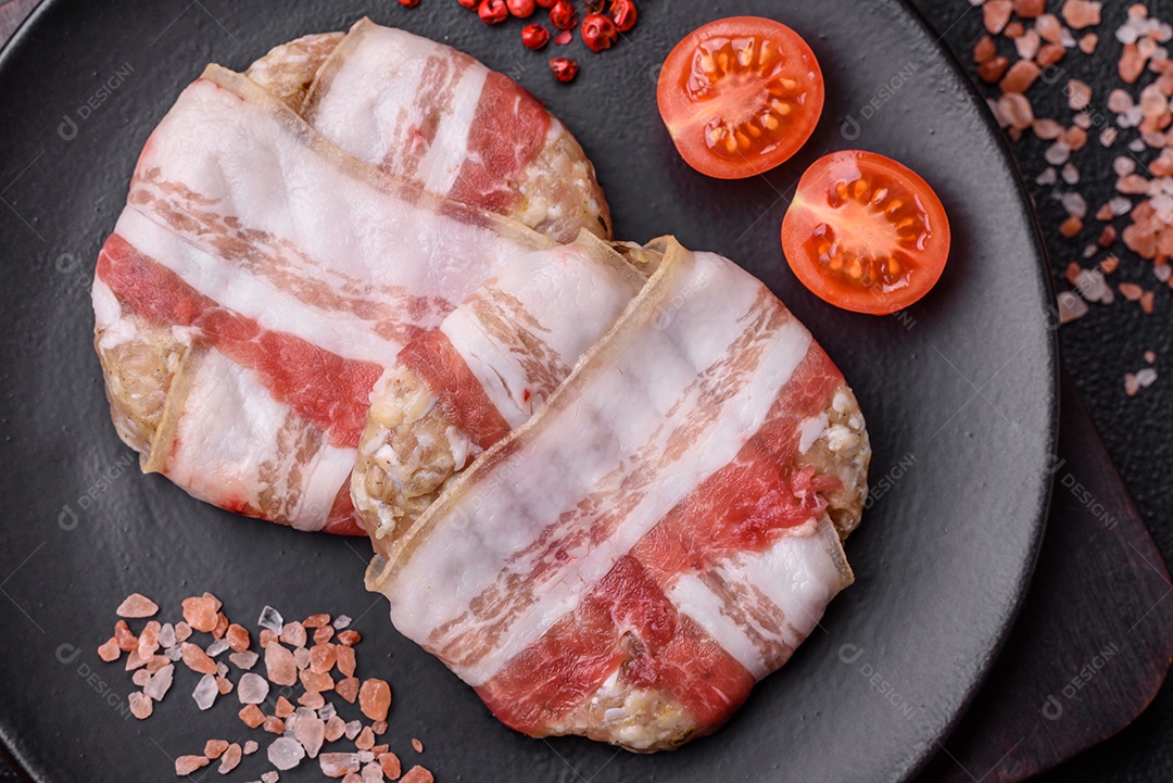 Frango picado redondo ou costeleta de porco envolta em bacon com sal, especiarias e ervas sobre um fundo escuro de concreto
