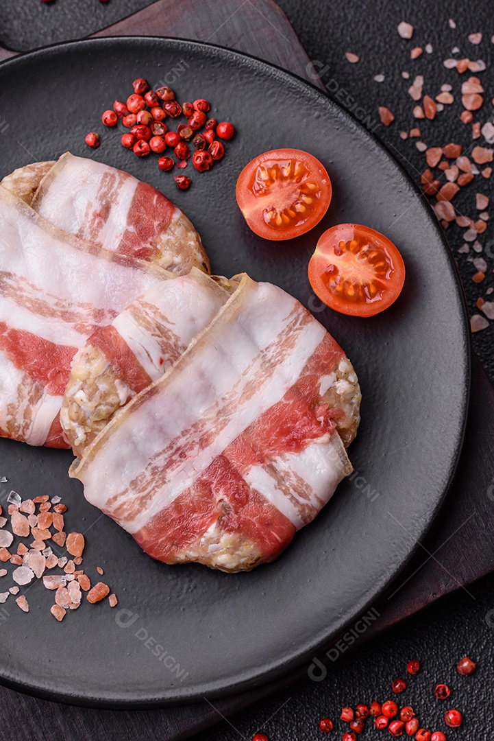 Frango picado redondo ou costeleta de porco envolta em bacon com sal, especiarias e ervas sobre um fundo escuro de concreto