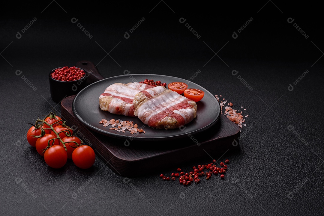 Frango picado redondo ou costeleta de porco envolta em bacon com sal, especiarias e ervas sobre um fundo escuro de concreto