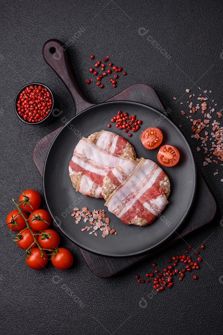 Frango picado redondo ou costeleta de porco envolta em bacon com sal, especiarias e ervas sobre um fundo escuro de concreto