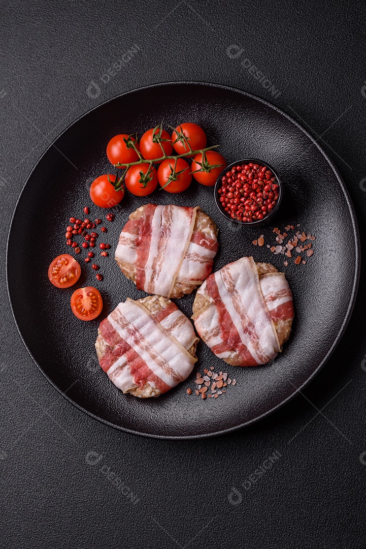 Frango picado redondo ou costeleta de porco envolta em bacon com sal, especiarias e ervas sobre um fundo escuro de concreto