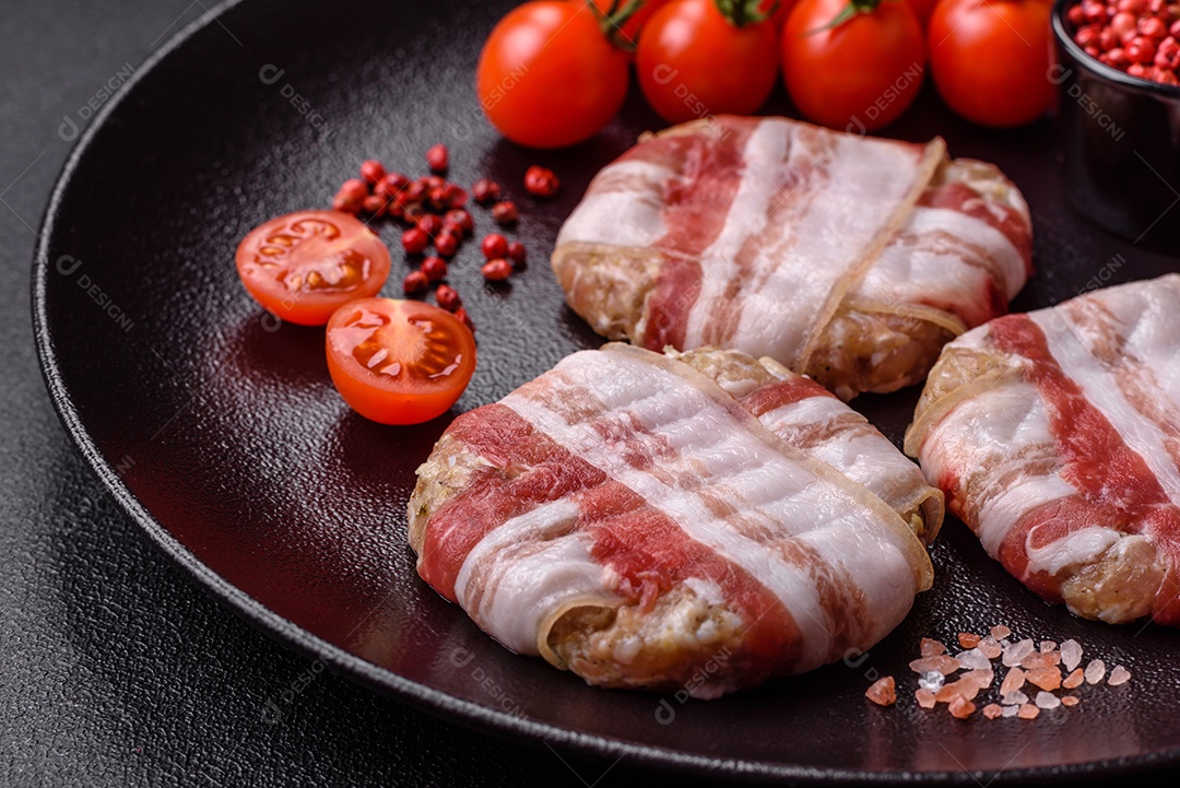 Frango picado redondo ou costeleta de porco envolta em bacon com sal, especiarias e ervas sobre um fundo escuro de concreto