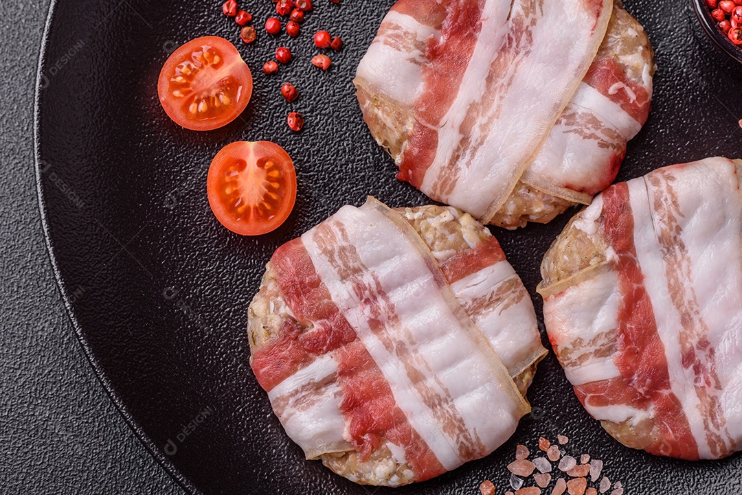 Frango picado redondo ou costeleta de porco envolta em bacon com sal, especiarias e ervas sobre um fundo escuro de concreto