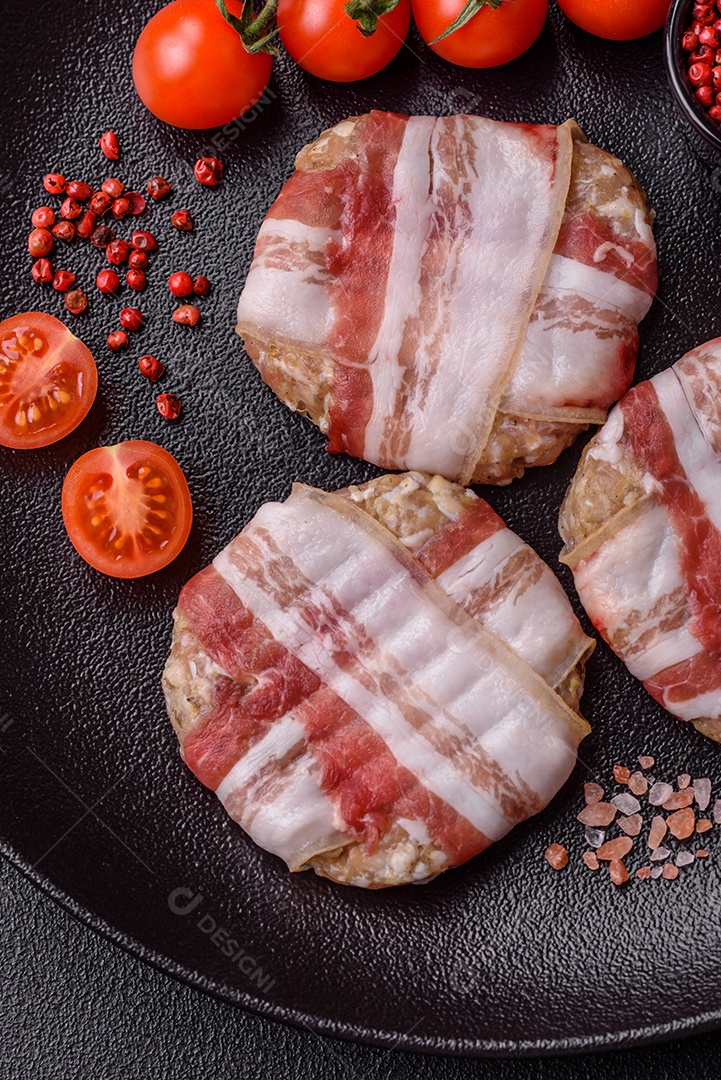 Frango picado redondo ou costeleta de porco envolta em bacon com sal, especiarias e ervas sobre um fundo escuro de concreto