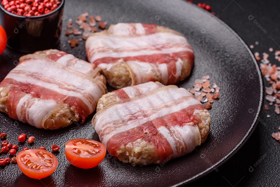 Frango picado redondo ou costeleta de porco envolta em bacon com sal, especiarias e ervas sobre um fundo escuro de concreto