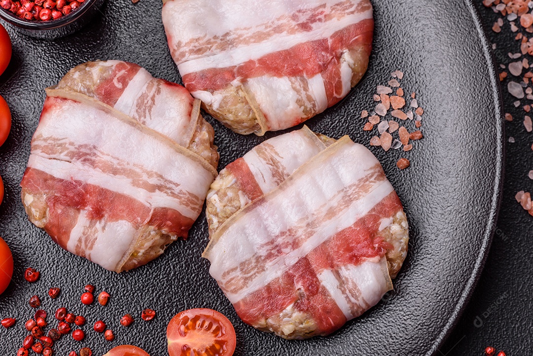 Frango picado redondo ou costeleta de porco envolta em bacon com sal, especiarias e ervas sobre um fundo escuro de concreto