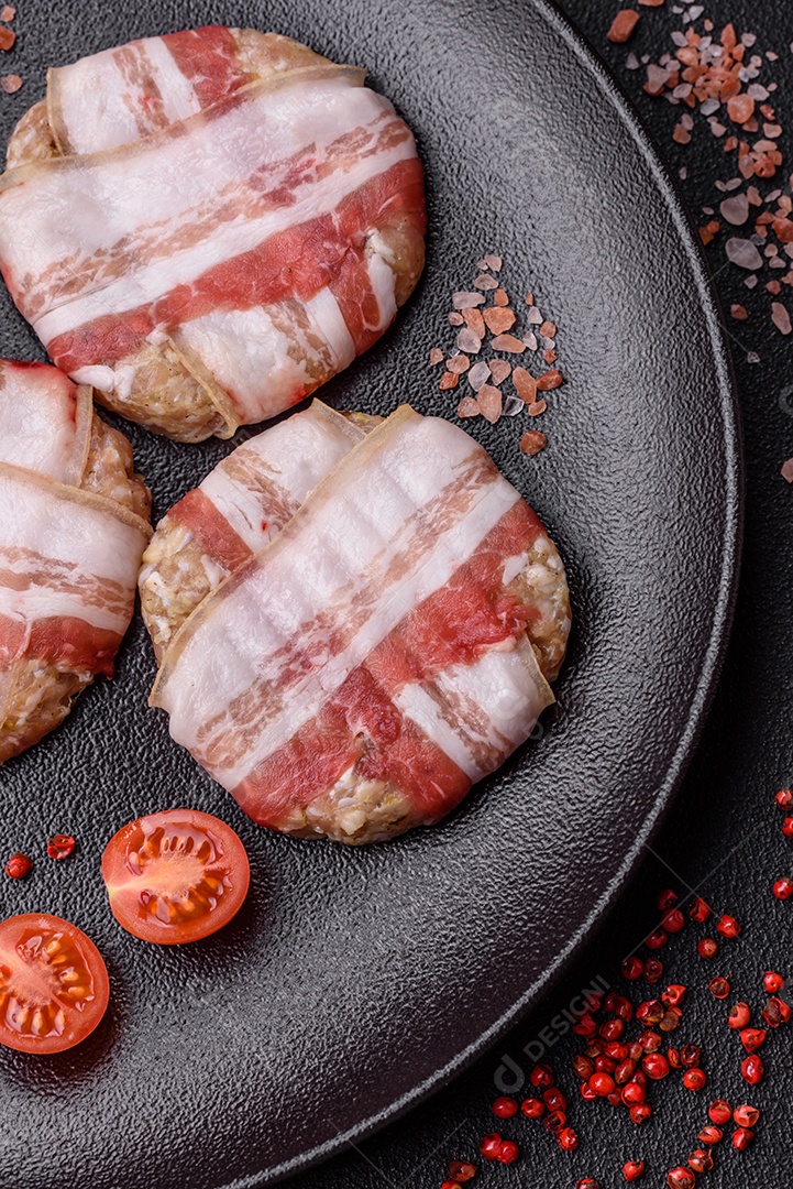 Frango picado redondo ou costeleta de porco envolta em bacon com sal, especiarias e ervas sobre um fundo escuro de concreto