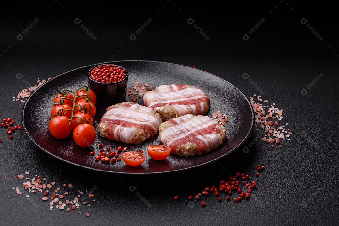 Frango picado redondo ou costeleta de porco envolta em bacon com sal, especiarias e ervas sobre um fundo escuro de concreto
