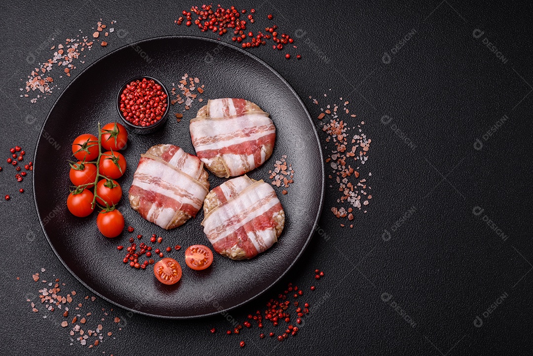 Frango picado redondo ou costeleta de porco envolta em bacon com sal, especiarias e ervas sobre um fundo escuro de concreto