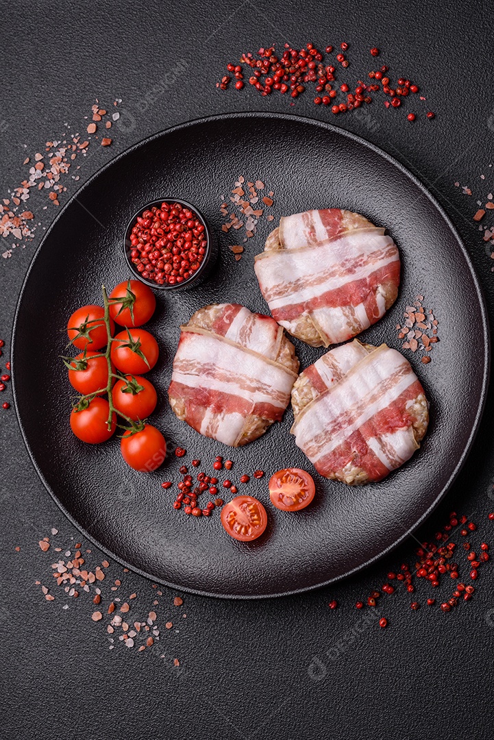 Frango picado redondo ou costeleta de porco envolta em bacon com sal, especiarias e ervas sobre um fundo escuro de concreto